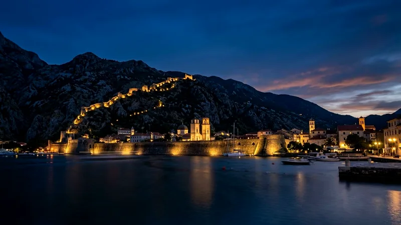 Kotor Old Town walls illuminated at dusk beneath a dark mountain